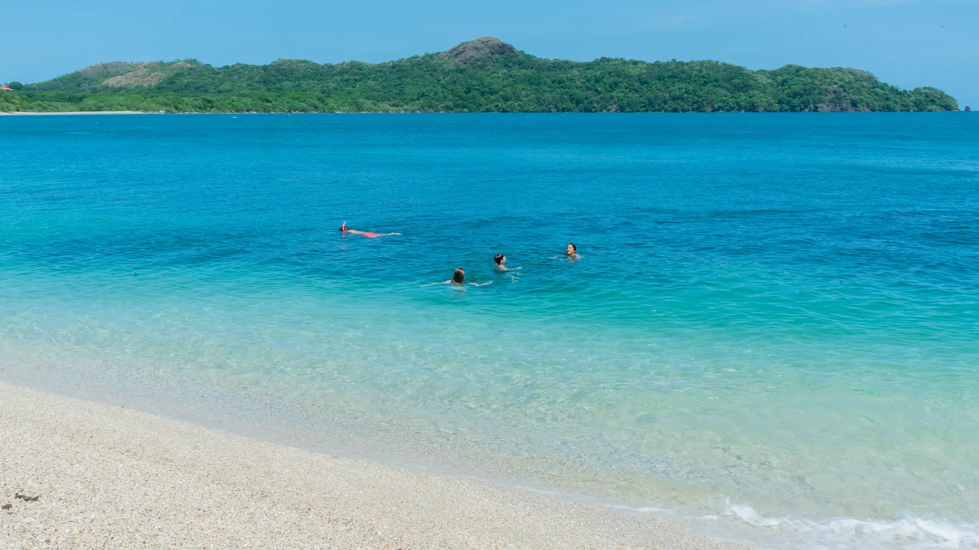 Swimmers floating in clear turquoise water near the white-sand beach