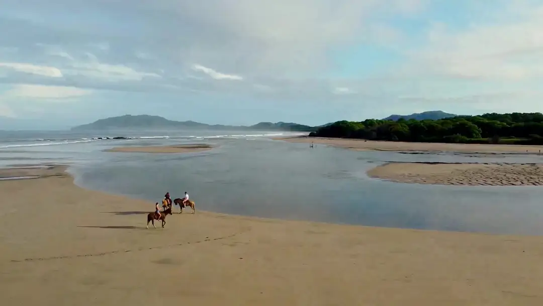 Riders on horseback crossing the wide beach at the Tamarindo estuary